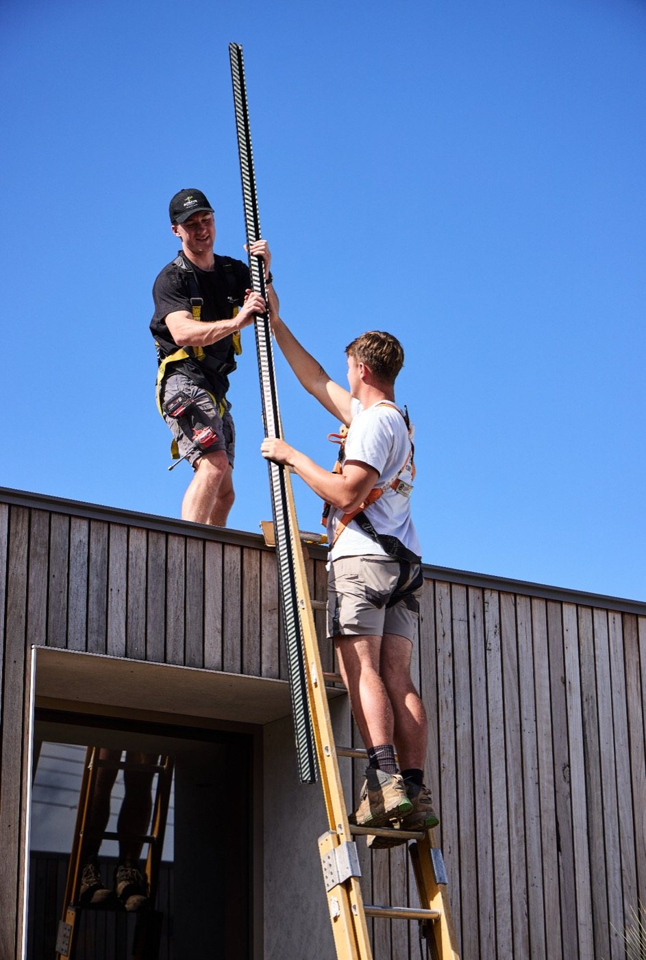 Two Ausave installers passing a mounting rail from a ladder up to the roof